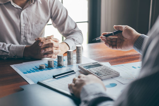 Wealth management advisors review investment performance charts, financial planning documents, stacked coins, and a calculator during a client portfolio discussion.